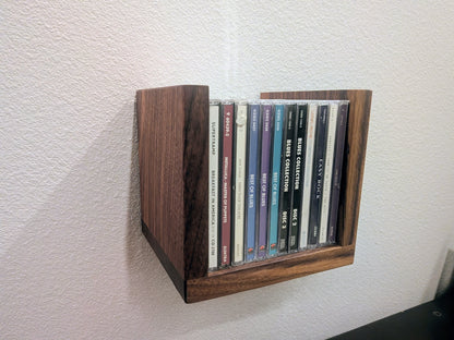 Wooden wall-mounted shelf with CDs on a white wall